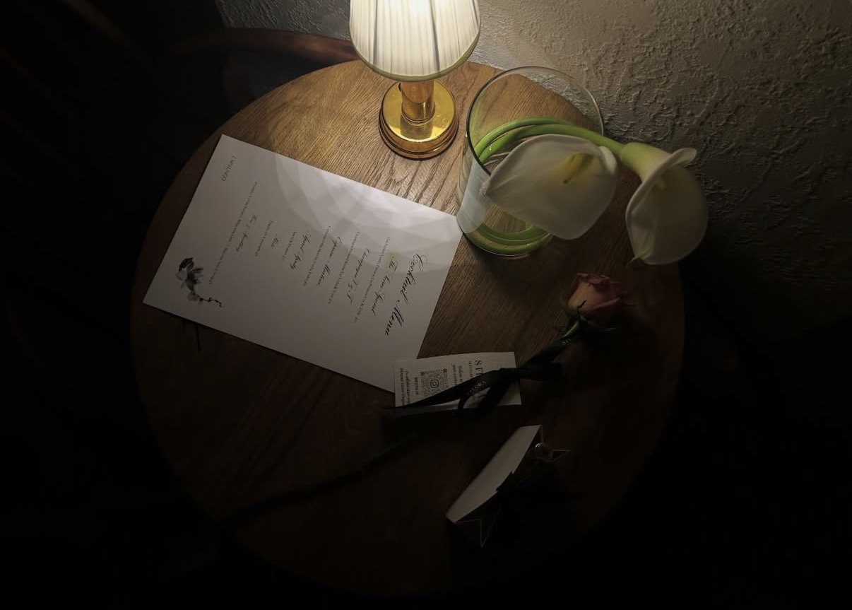Cocktail menu and a rose on a table by lamplight